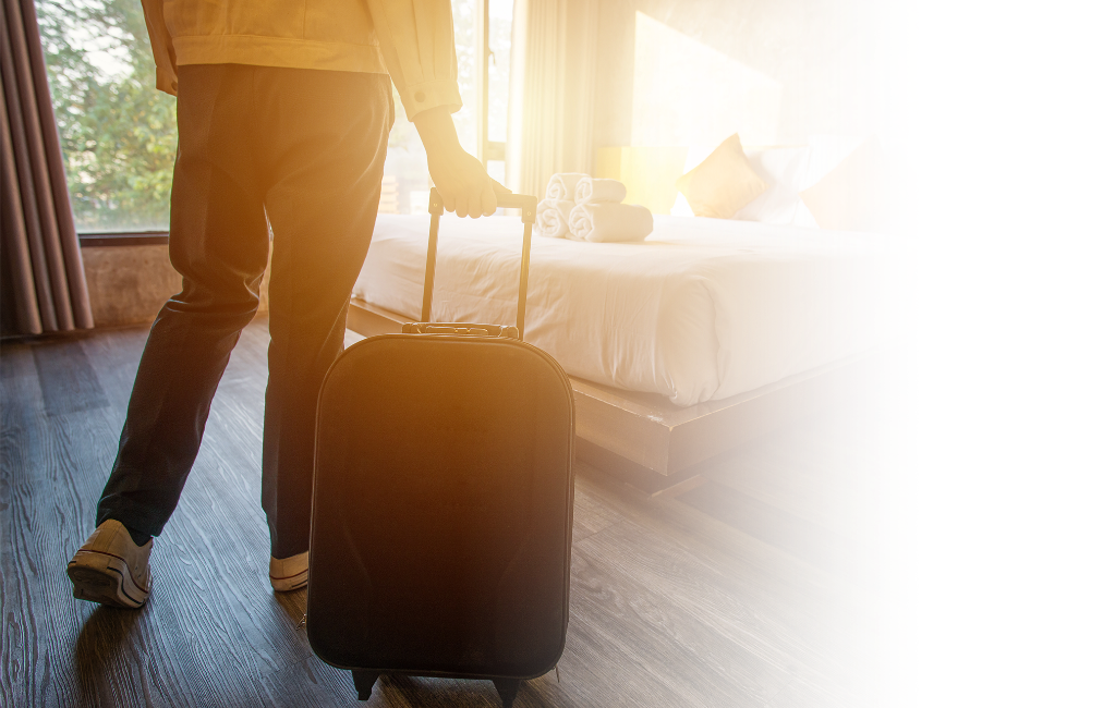 A person walking into a hotel room pulling a suit case.